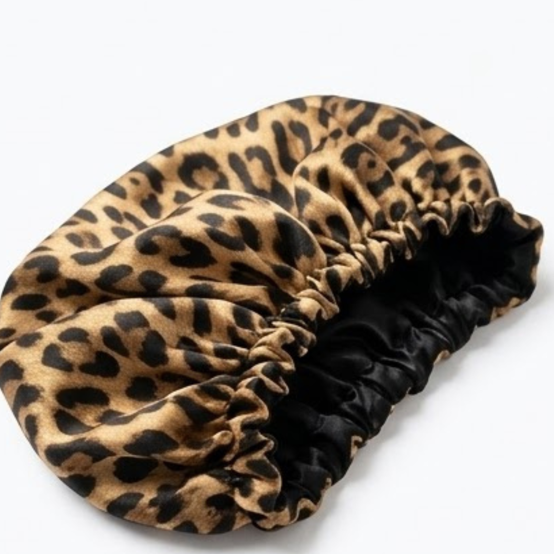 Touca de Cetim de Leopardo Antifrizz Touca de cetim com padrão de leopardo e interior preto, pousada num fundo branco limpo, para cuidado do cabelo e redução do frizz.