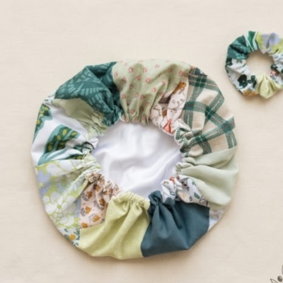 Uma foto de estúdio de uma touca de cetim e scrunchie combinando em tecido de retalhos verde e floral.