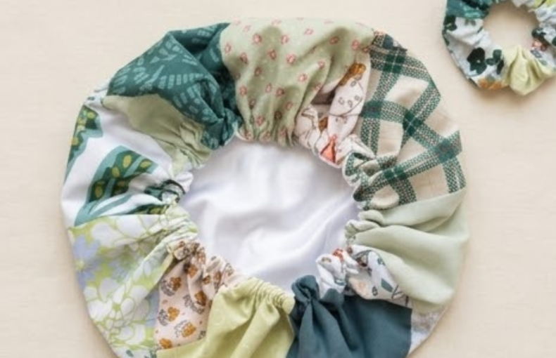 Uma foto de estúdio de uma touca de cetim e scrunchie combinando em tecido de retalhos verde e floral.