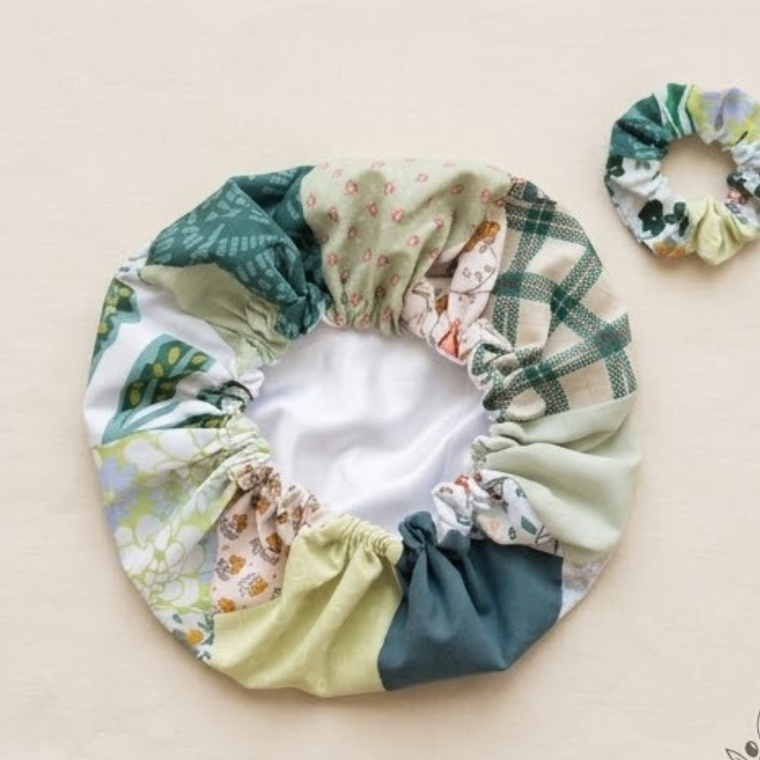 Uma foto de estúdio de uma touca de cetim e scrunchie combinando em tecido de retalhos verde e floral.