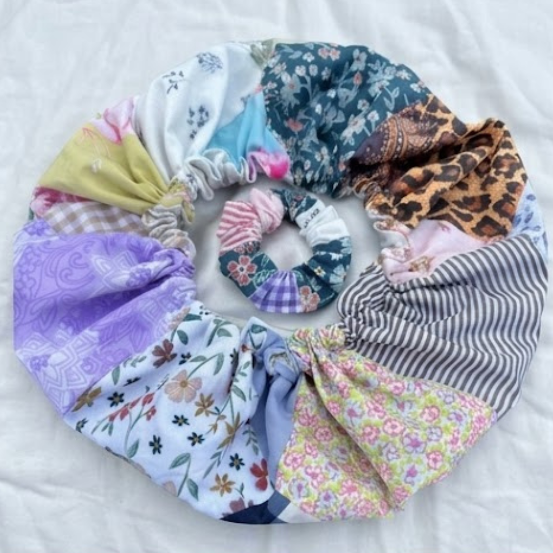 Vista de cima de um conjunto capilar artesanal composto por uma touca de cetim e um scrunchie em patchwork, exibindo um mix vibrante de estampas como leopardo, floral, riscas e xadrez sobre um fundo branco.