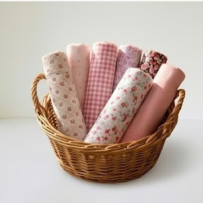 "Quatro imagens combinadas mostrando um cesto de vime com rolos de tecidos artesanais em tons de rosa, branco e floral. Os tecidos têm padrões de mini flores, xadrez gingham e motivos românticos, apresentados sobre diferentes fundos: azul texturado, cinza minimalista, mármore elegante e um estúdio claro e neutro."